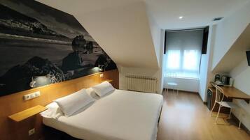 Una habitación de hotel con una cama, un escritorio, una silla, un radiador y un cuadro grande en la pared.