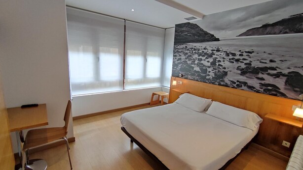 Habitación de hotel con una cama grande, un escritorio, una silla y un ventanal con cortinas.