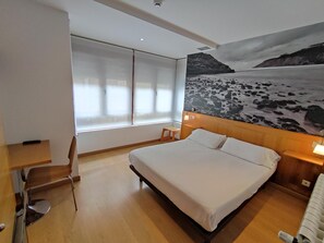 A hotel room with a large bed, a desk, a chair, and a window with curtains. - Hotel Dabeleira (Valdes)