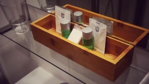Una caja de madera con artículos de aseo personal sobre un estante de vidrio en un baño.