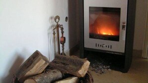 A wood-burning stove with logs in front, a decorative key on a wall-mounted ornament, and a tiled floor.