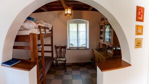 A cozy room with a bunk bed, a chair, a small table, a cabinet, and a window with curtains.