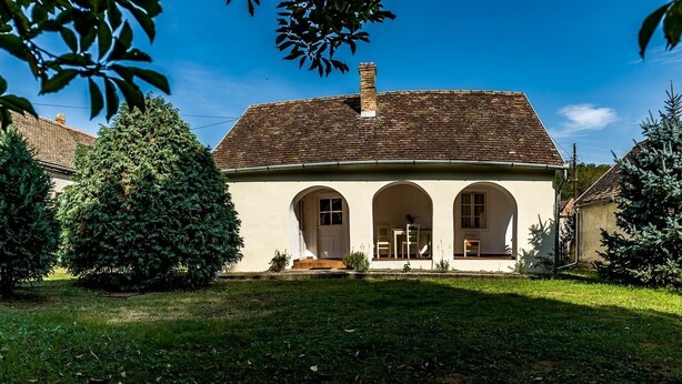 A two-story building with a tiled roof, a central entrance with three arches, and a small porch area.