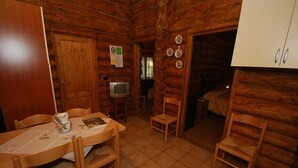 A log cabin interior with a dining area, a television, and a bed.