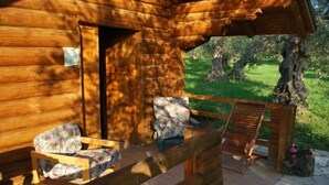 A wooden cabin with a porch, two floral-patterned chairs, and a wooden bench.