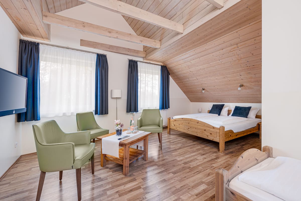 A bedroom with a wooden ceiling, a bed, a table with chairs, and a TV mounted on the wall.
