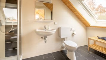 Een moderne badkamer met dakraam, een witte wastafel, toilet en een houten plank.
