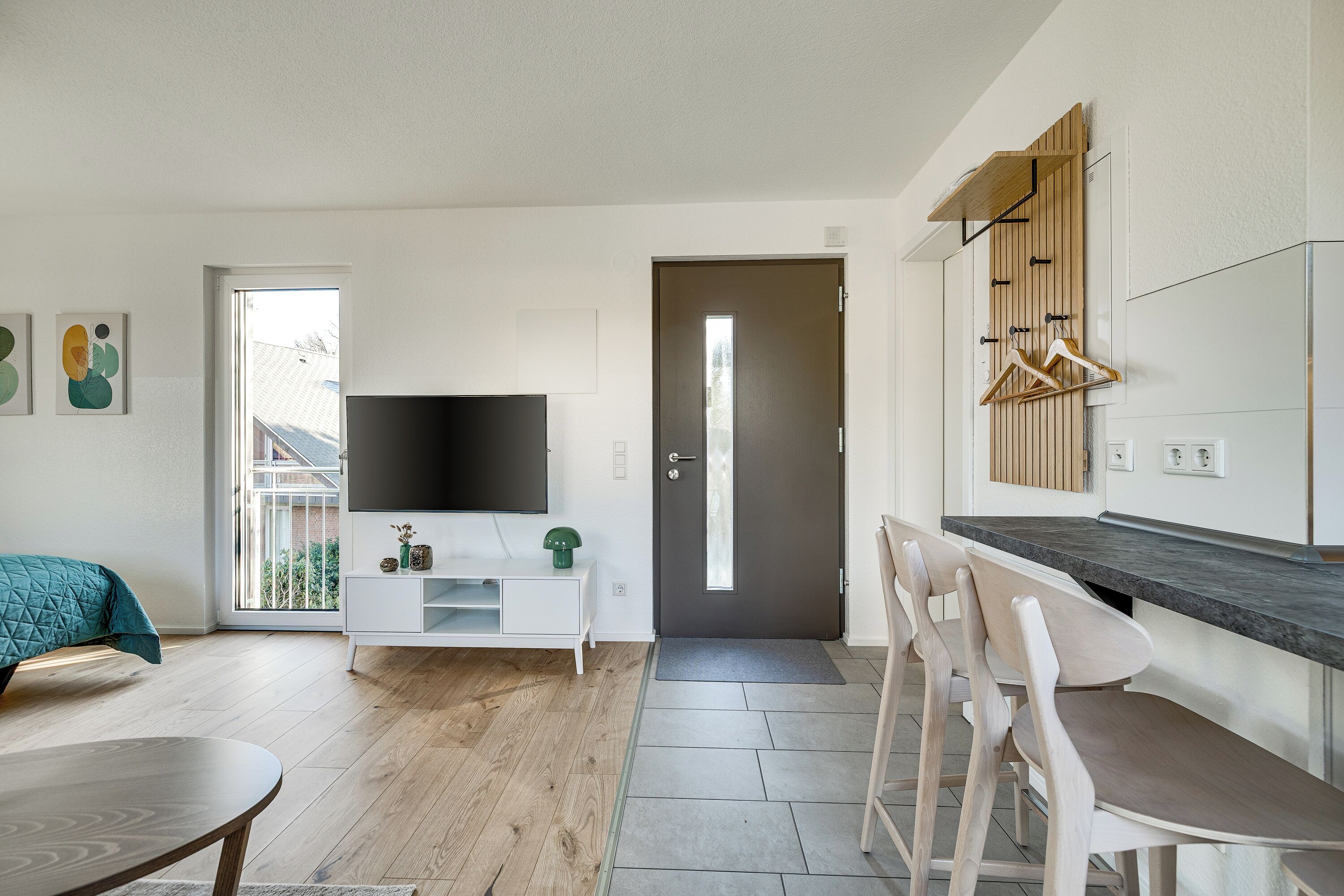 Una sala de estar moderna con televisor, un comedor con sillas, una cocina con mostrador y una puerta que da al exterior.