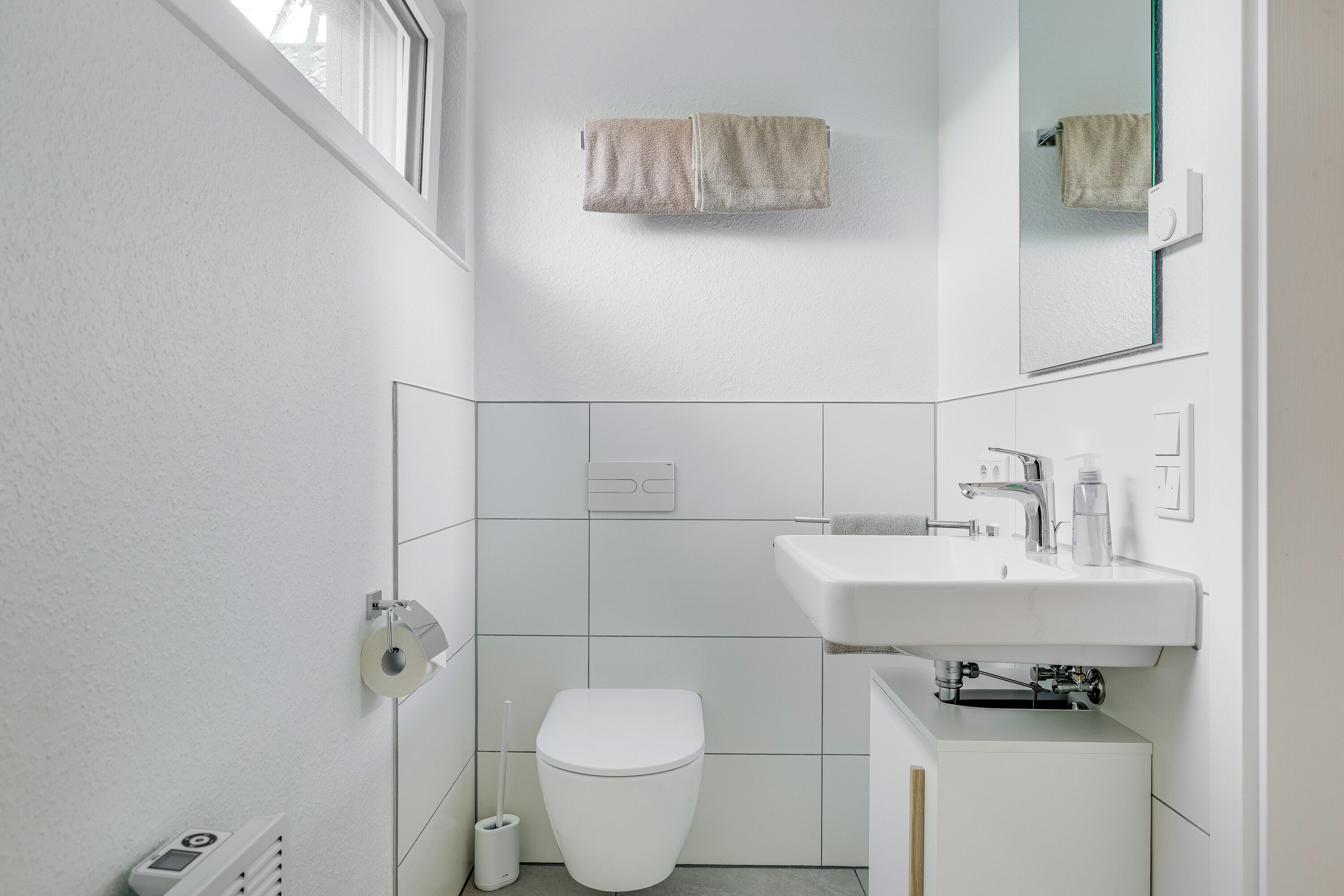 A modern bathroom with a toilet, sink, and towel hanging on the wall.