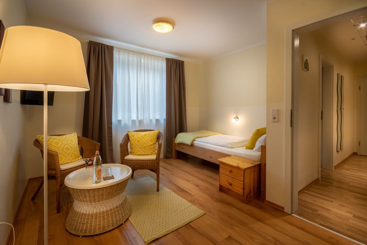 A hotel room with a bed, a chair, a small table, a lamp, and a window with curtains.