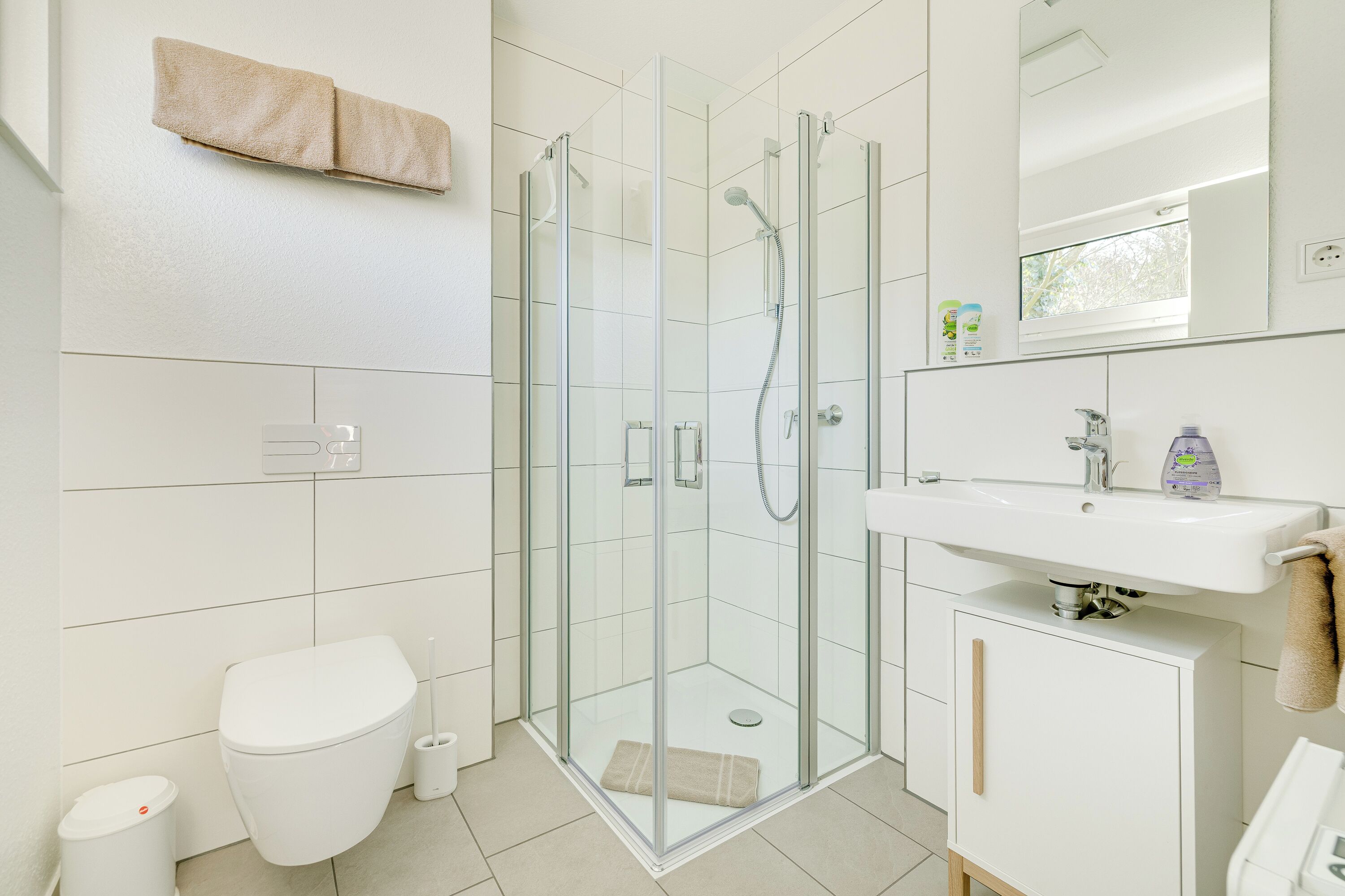 Un baño moderno con ducha de vidrio, inodoro blanco y lavamanos con espejo.
