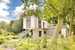 A modern two-story house with a balcony, surrounded by lush greenery and flowering plants. - Haus Biederstaedt (Ottersberg)