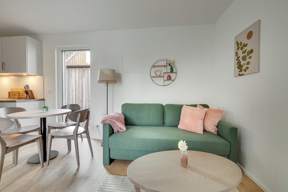 A modern living room with a green sofa, a round coffee table, and a dining area with a table and chairs.