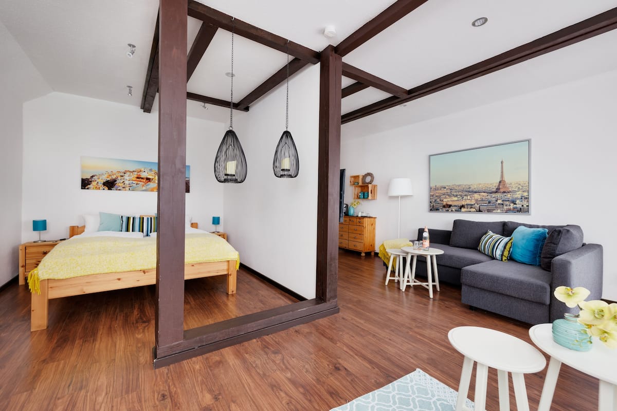 A modern bedroom with a wooden bed, a gray sofa, and a cityscape painting.