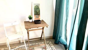 Une petite table en bois, sur laquelle sont posés un pot de fleurs et un panier, une chaise blanche et un miroir accroché au mur.