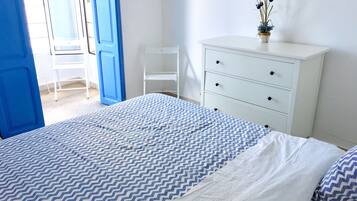 Een slaapkamer met een bed, een witte dressoir, een stoel en een bloempot.
