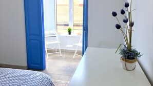 Une chambre avec un lit, une petite table sur laquelle est posée une plante en pot, et un balcon avec des chaises et une table.