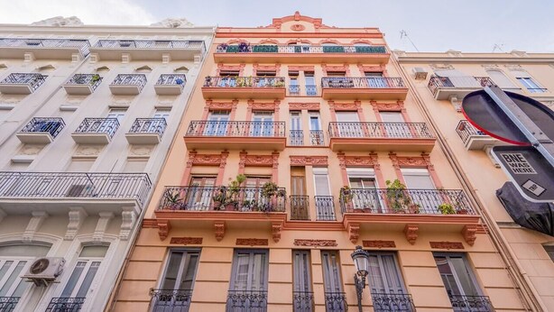 Un immeuble à plusieurs étages doté de balcons, d’une horloge et d’une enseigne indiquant un ancien emplacement.