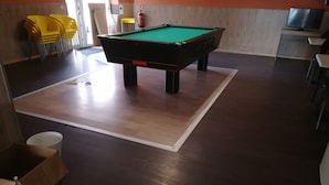 A pool table in a room with wooden flooring, yellow chairs, and a fire extinguisher. - Logies Waasland (Sint-Niklaas)