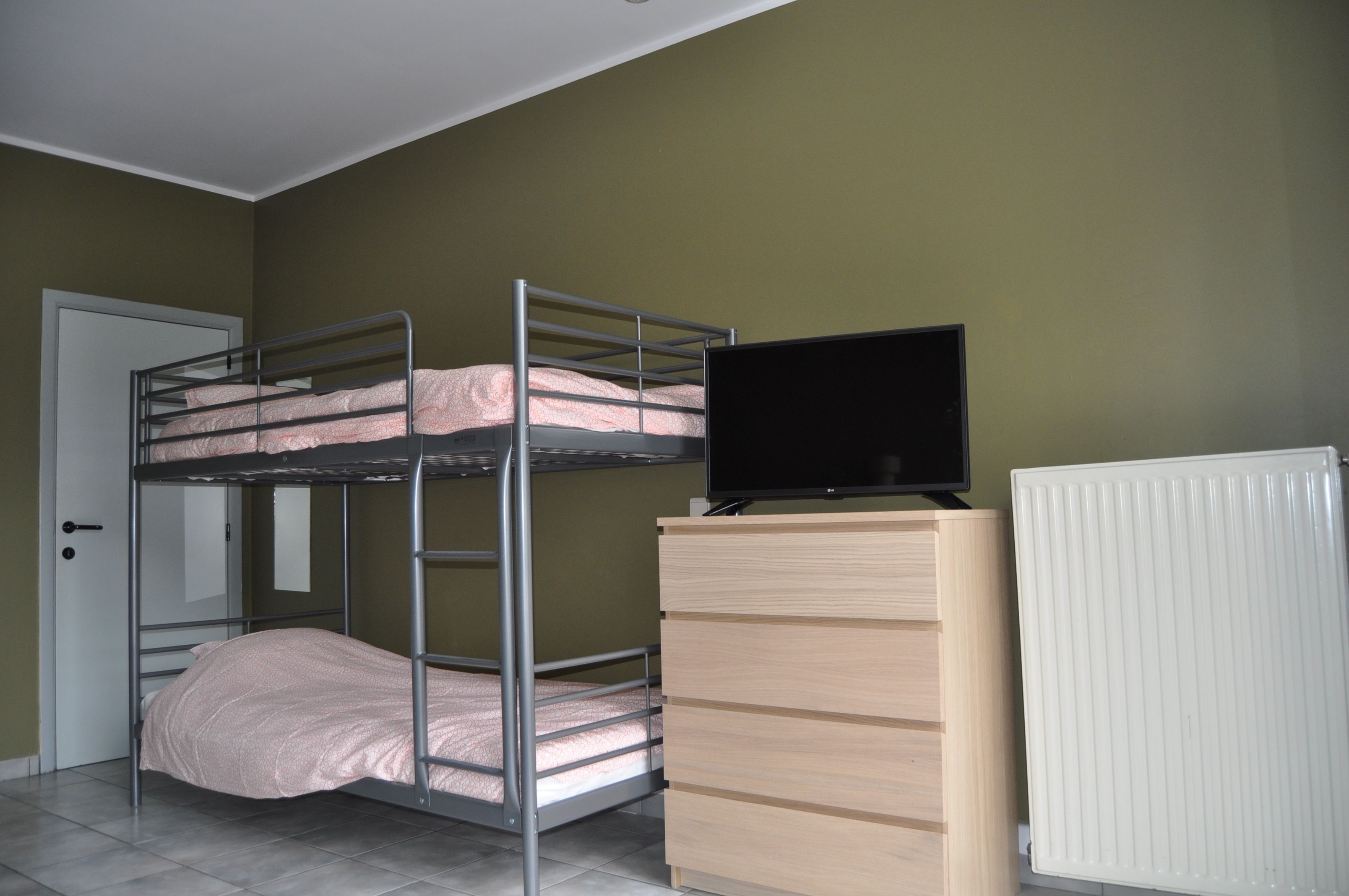 Un lit superposé avec un téléviseur en haut, une commode et un radiateur.