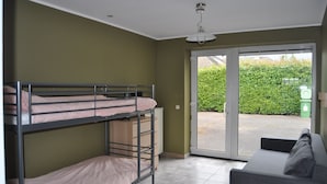 A dormitory room with bunk beds, a sofa, and a sliding glass door leading to an outdoor area. - Logies Waasland (Sint-Niklaas)