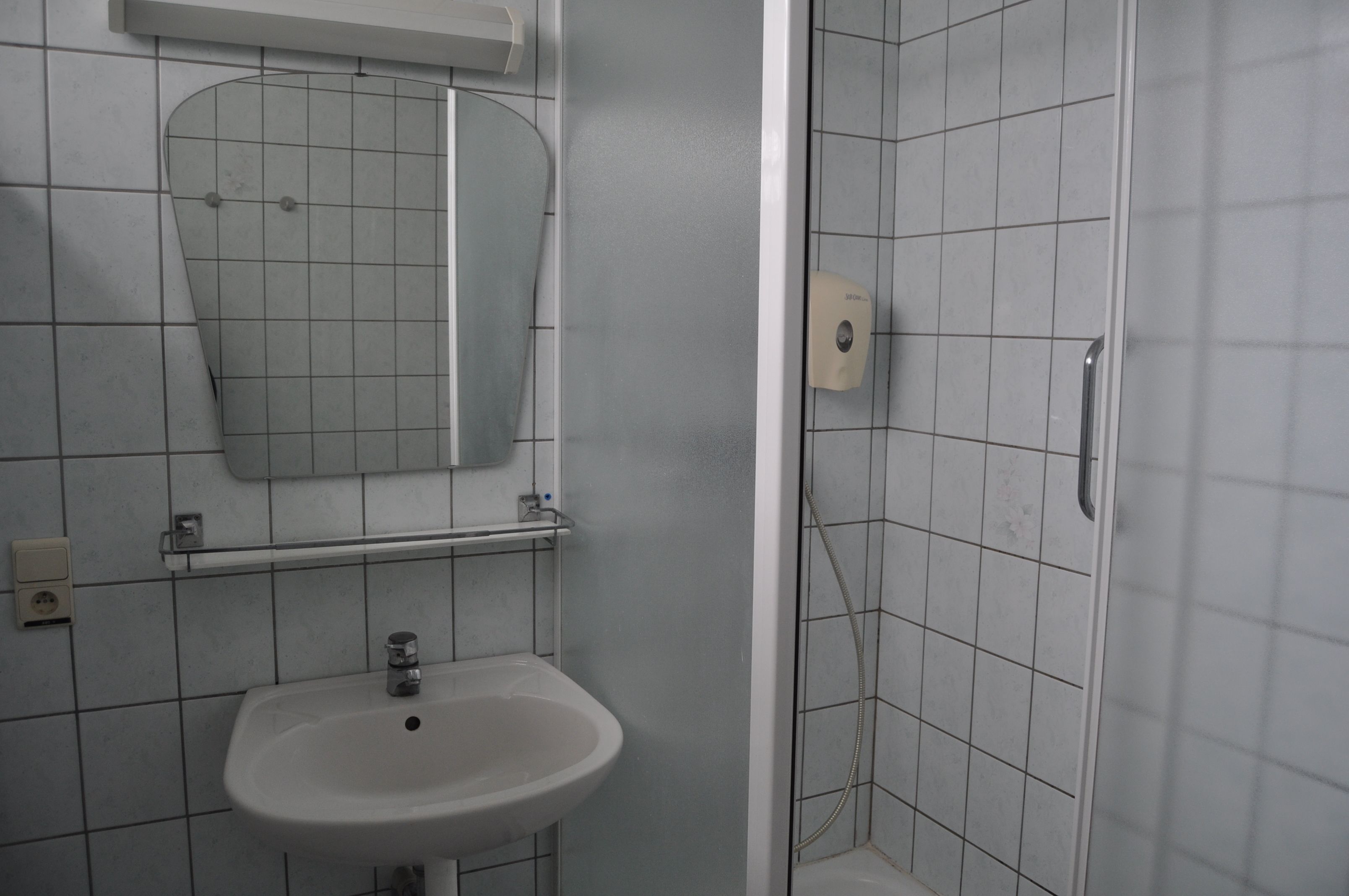 A bathroom with a white sink, a mirror, and a shower area.