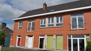 A two-story brick house with a red door, large windows, and a balcony. - Logies Waasland (Sint-Niklaas)