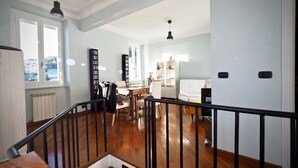Un espacio habitable amplio con piso de madera, un sofá blanco, una mesa de comedor y una estantería.