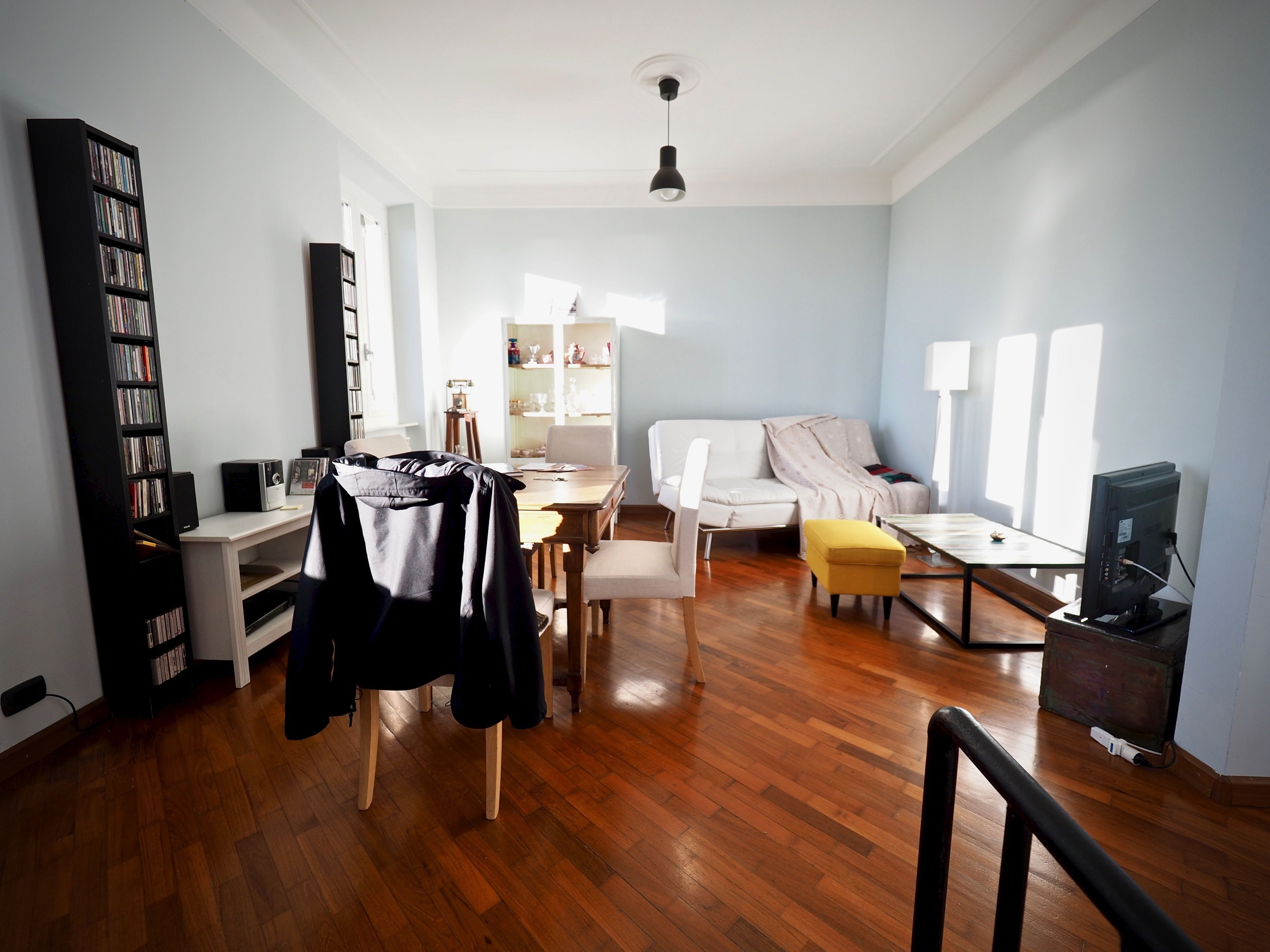 A spacious living room with a wooden floor, a white sofa, a coffee table, and a bookshelf.