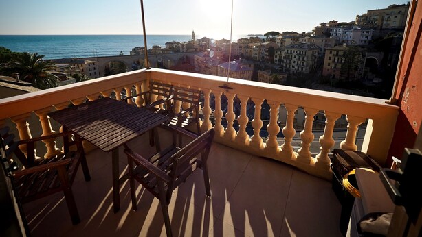 Un balcón con mesa y sillas, con vista a un pueblo costero con edificios y el mar.