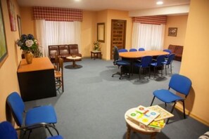 Une salle de conférence avec une longue table, des chaises bleues, une petite table d’appoint avec des livres et une bibliothèque.