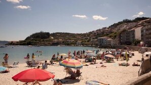 Una playa con gente tomando el sol y nadando, sombrillas y edificios al fondo.