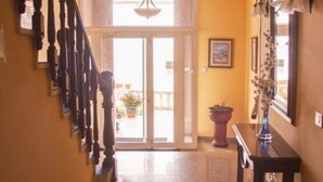 Un pasillo con una escalera a la izquierda, una puerta al final y una planta en maceta a la derecha.