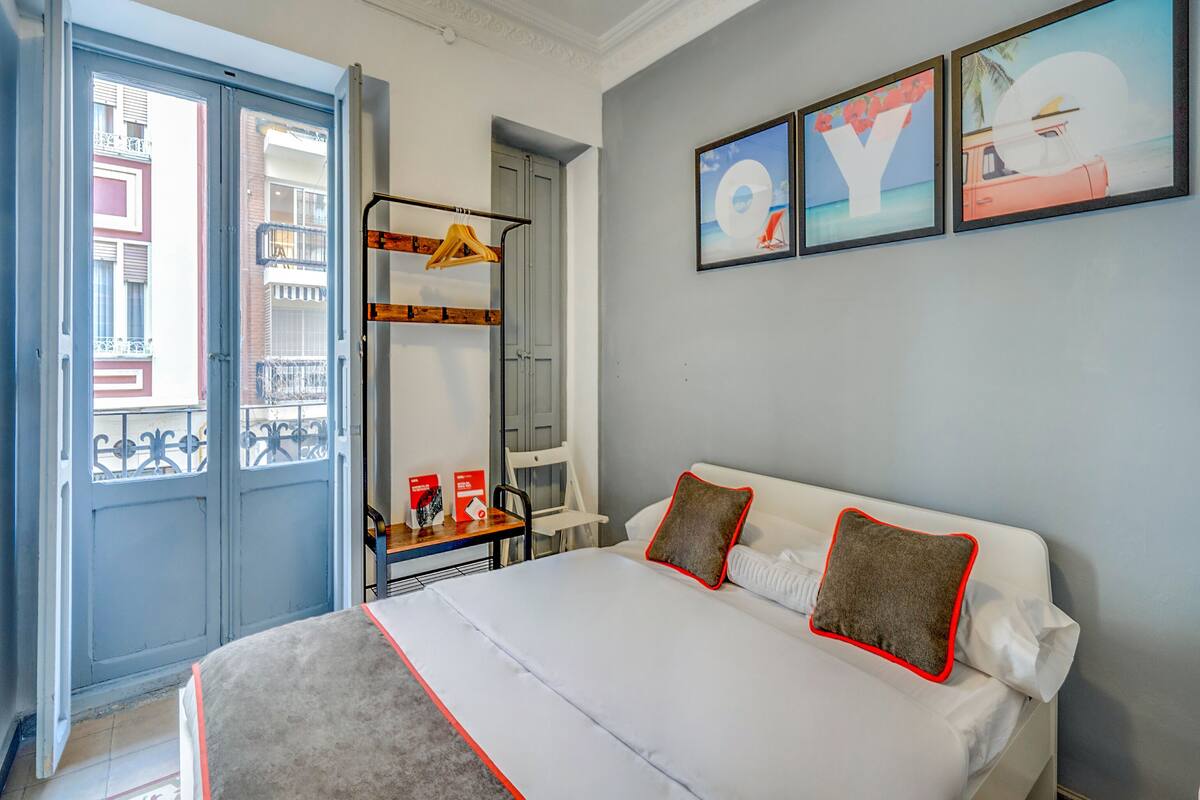 A bedroom with a bed, pillows, a hanging rack, and a view of the outside.