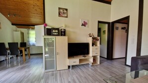 Een moderne woonkamer met een houten plafond, een glazen salontafel, een tv-meubel en een eethoek met stoelen en een tafel.