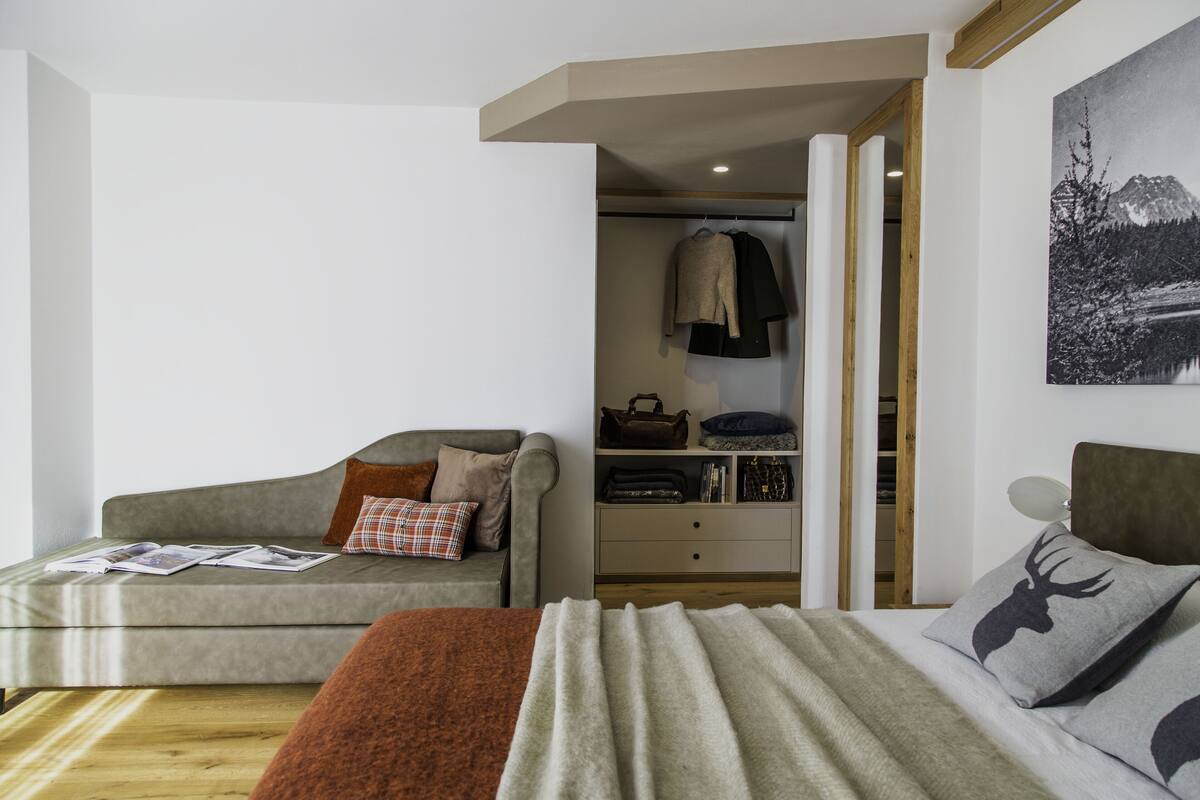 A modern bedroom with a grey sofa, a bed with a grey and brown blanket, and a wooden floor.