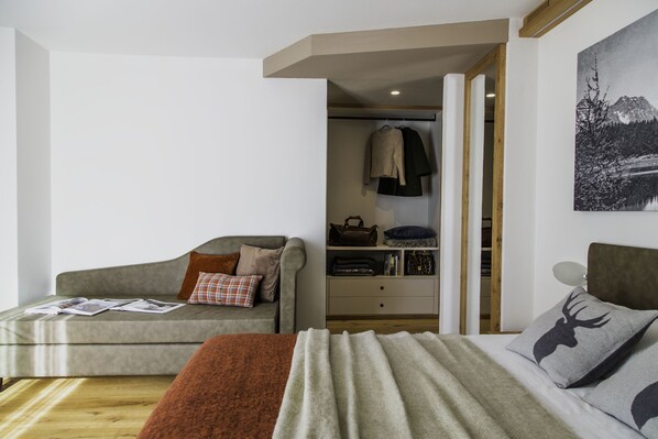 Une chambre moderne avec un canapé gris, un lit recouvert d’une couverture grise et marron, et un plancher en bois.