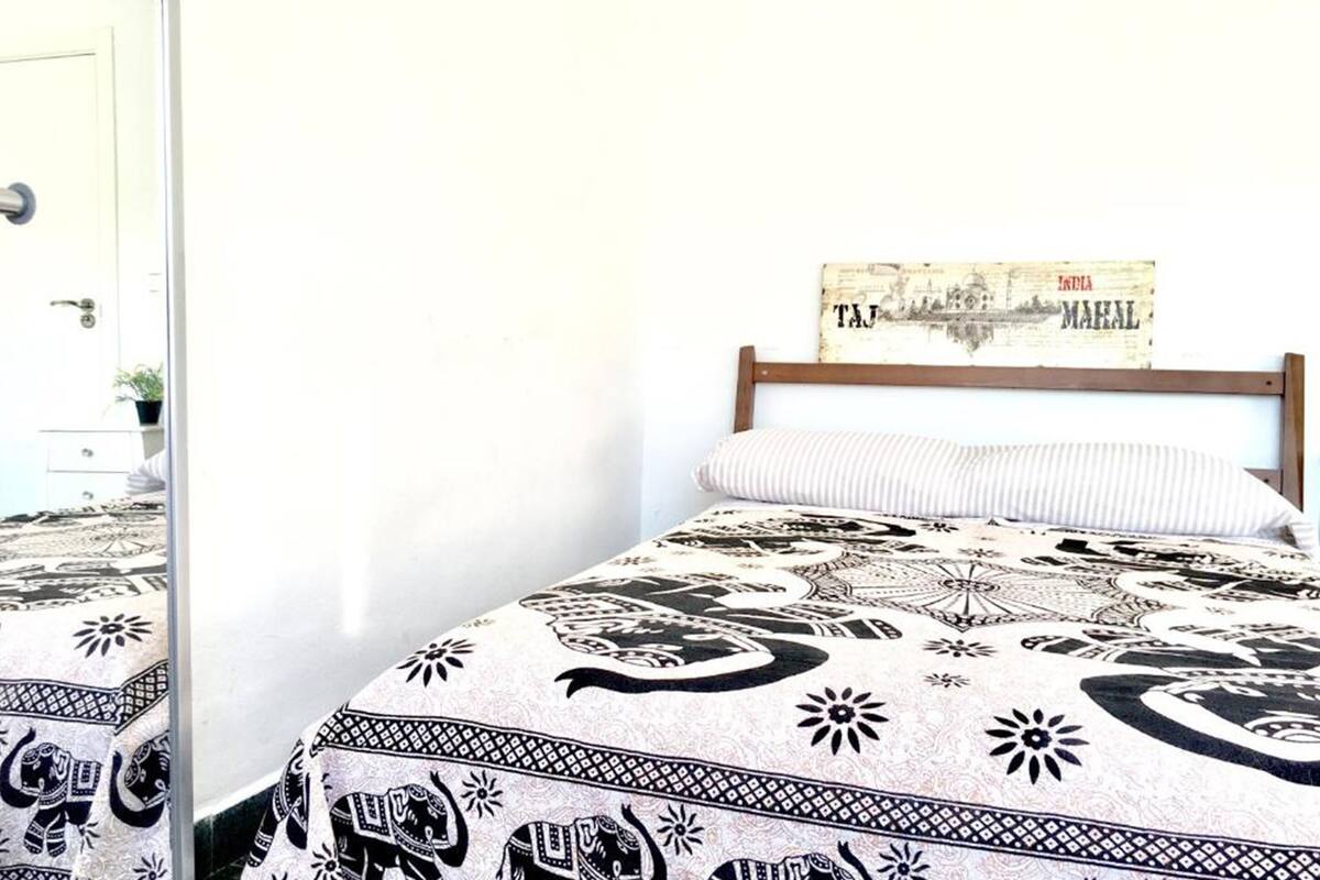 Un lit avec une couvre-lit à motifs, une tête de lit en bois et un panneau mural portant les mots « Inde » et « Taj Mahal ».