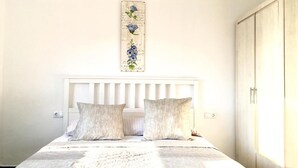 A bedroom with a white headboard, a bed with a patterned bedspread, and a wall-mounted decorative piece. - OYO Guest House Torre de Quart (Valencia)