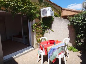 Une terrasse extérieure avec une table et des chaises, un appareil de climatisation et une porte-fenêtre coulissante donnant sur un espace abrité.