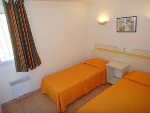 Une chambre avec deux lits, une petite table de chevet, une lampe fixée au mur et une fenêtre avec des rideaux.