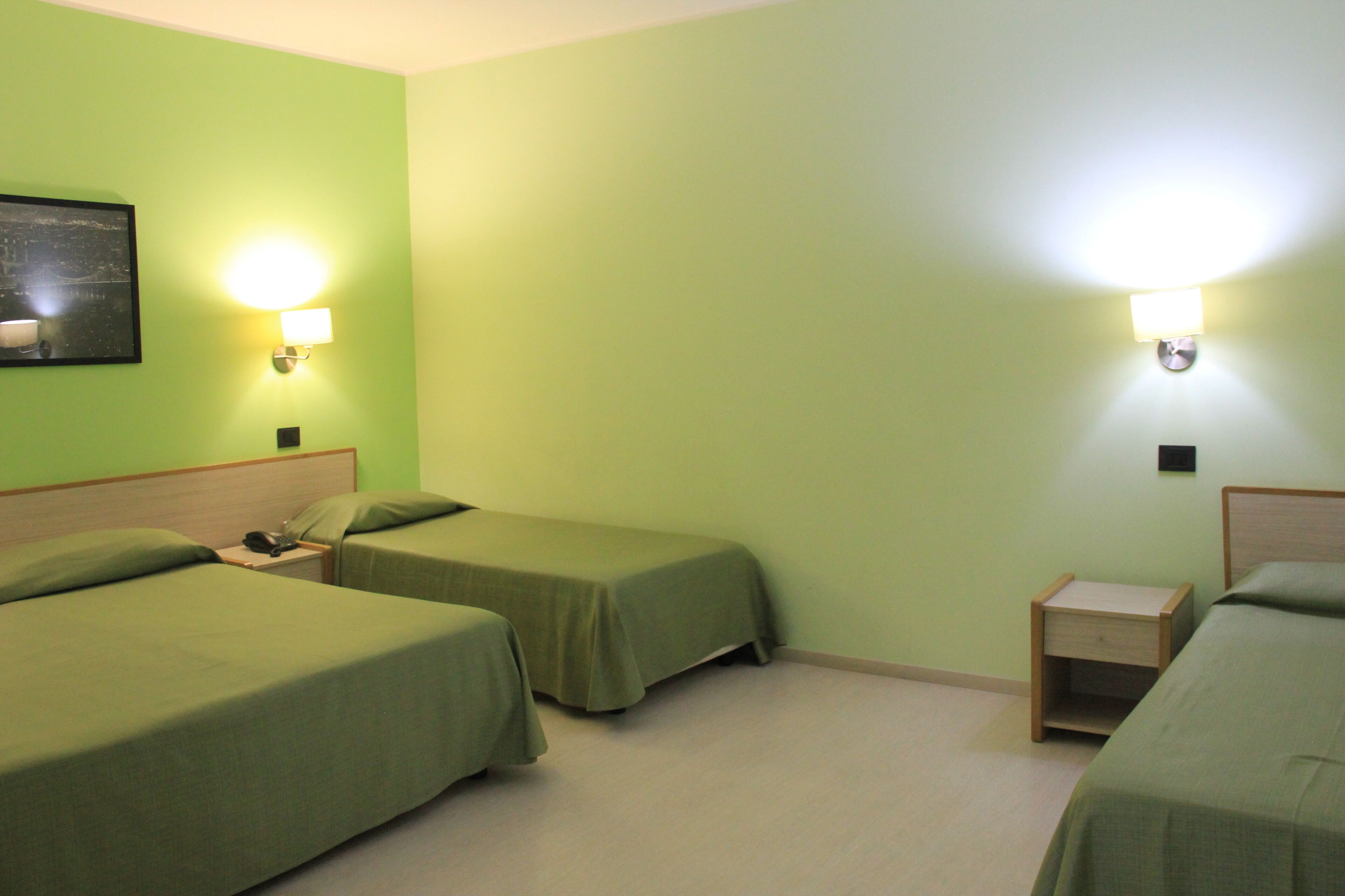 A room with two single beds, a nightstand with a lamp, and a small wooden drawer unit.