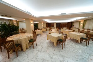 Enjoy meals in this elegant dining area with high ceilings and skylights, set with white tablecloths and green cushioned chairs.