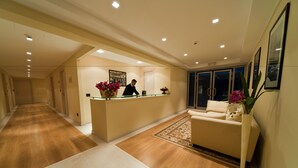 A hotel reception area with a reception desk, a receptionist, a sofa, and a vase with flowers. - Hotel Città dei Papi (Anagni)