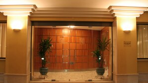 A hotel entrance with a wooden reception desk, two potted plants, and a reception area with a light fixture. - Hotel Città dei Papi (Anagni)