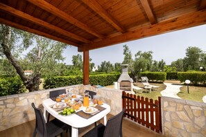 Eine Außenpatio mit Steinmauern, einer Holzbeschichtung und Blick auf einen Garten mit Grillplatz.