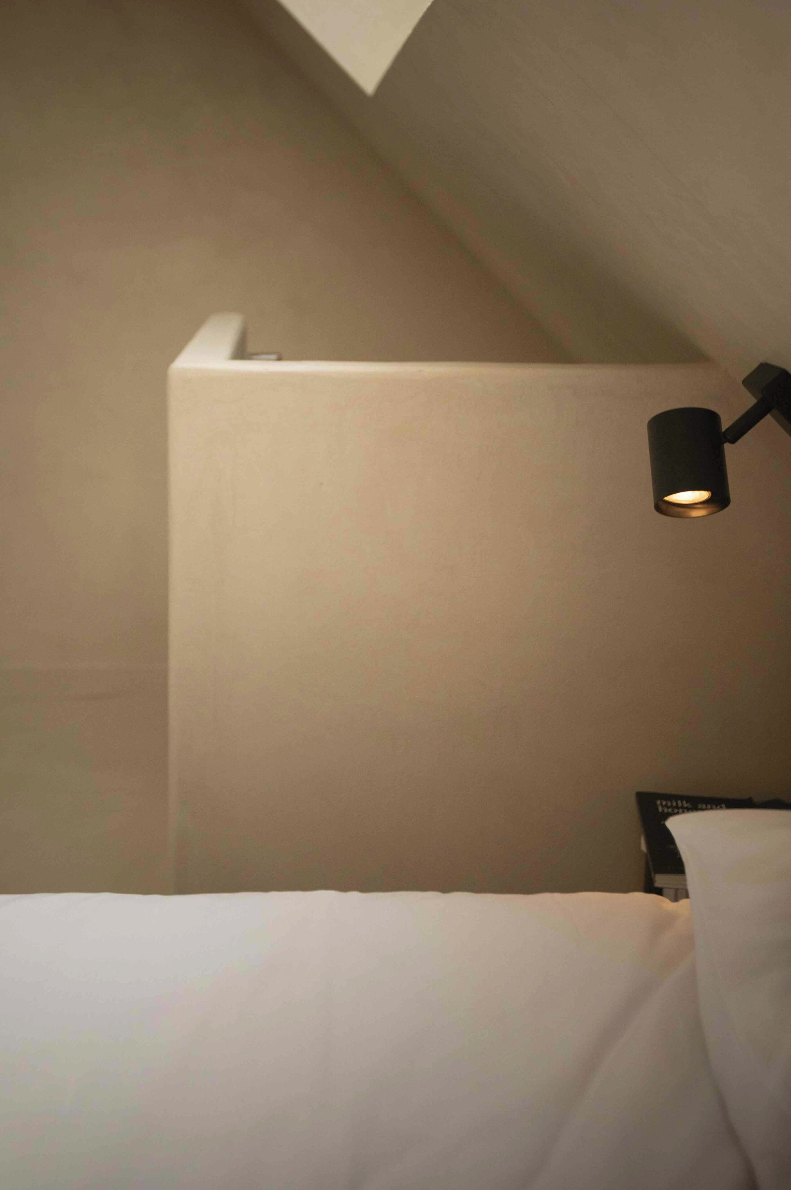Een slaapkamer met een schuine kap, een enkel bed en een wandlamp.