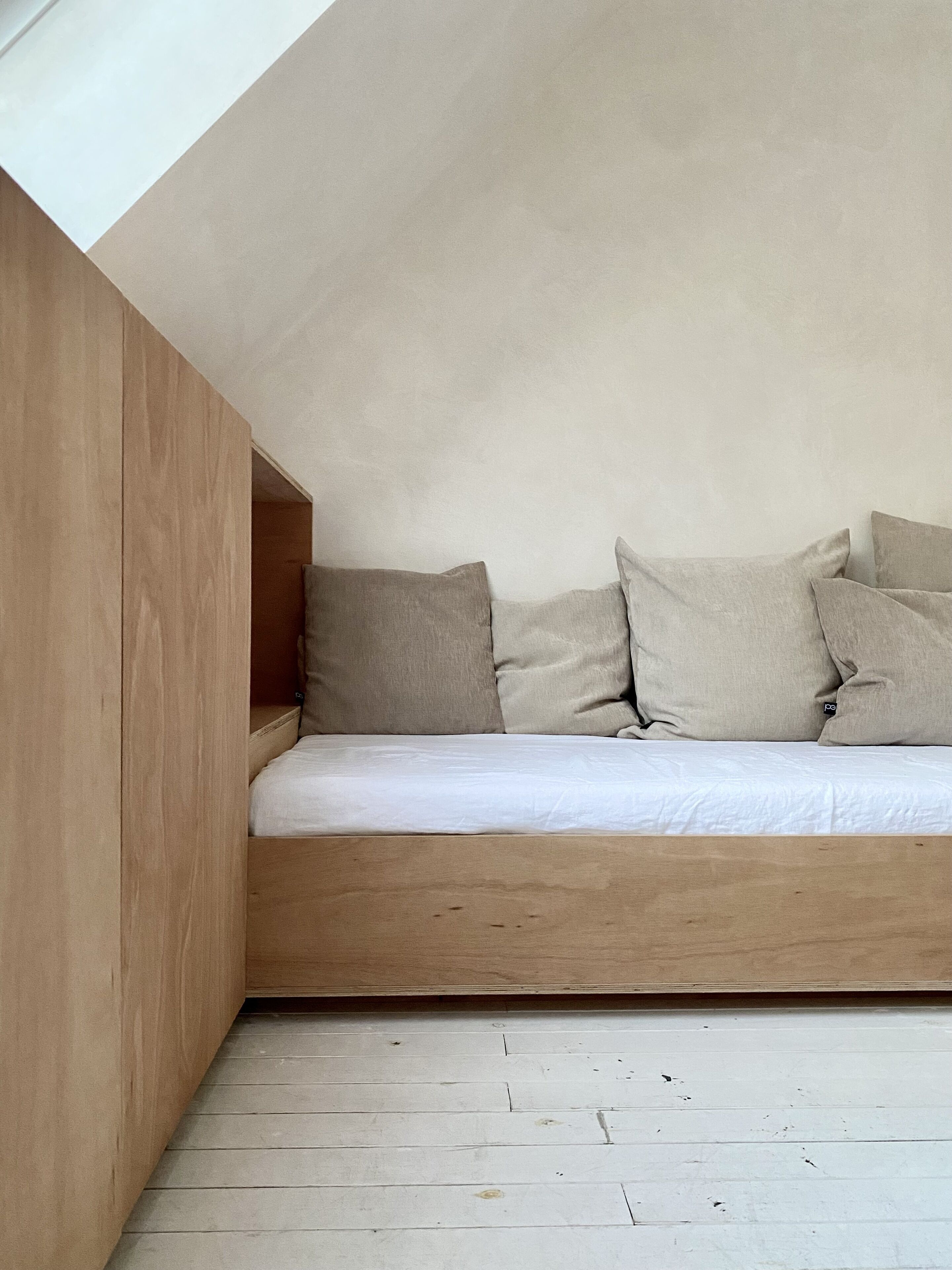 Een slaapkamer in loftstijl met een houten platformbed, wit beddengoed en een schuin dak.