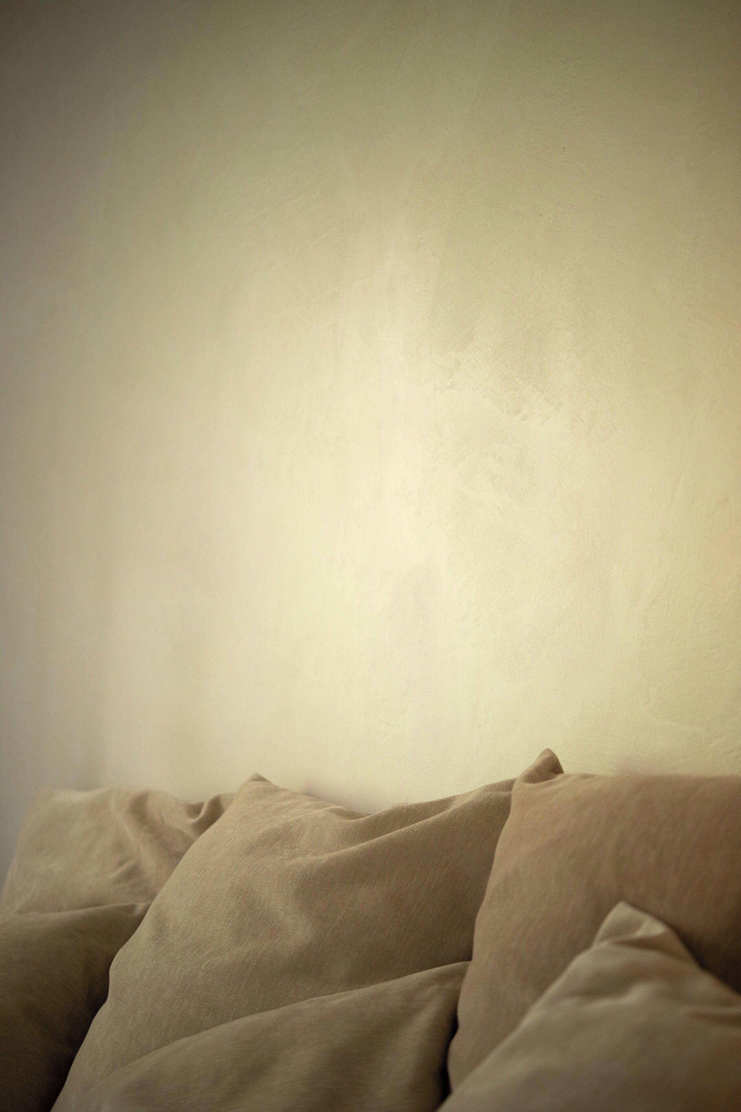 Una habitación con una pared sencilla y una cama con ropa de cama color beige.