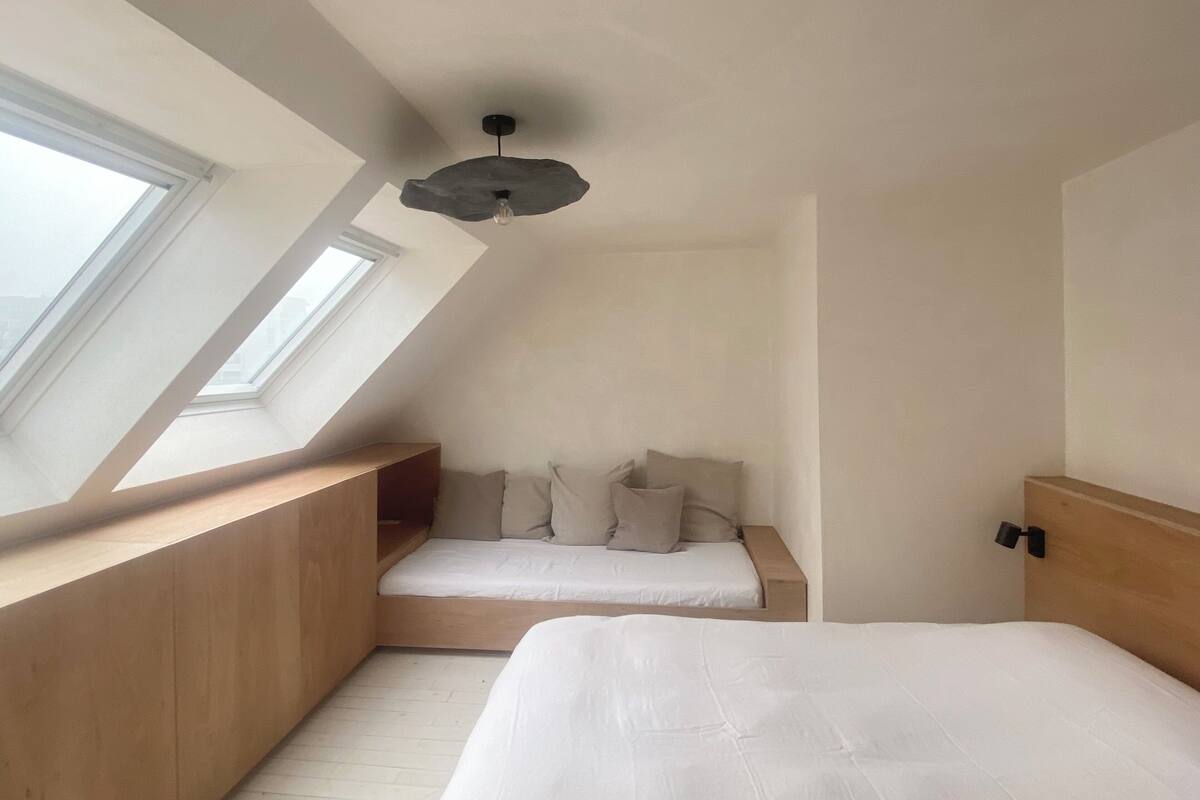 A bedroom with a sloped ceiling, skylight, two beds, and a wooden headboard.
